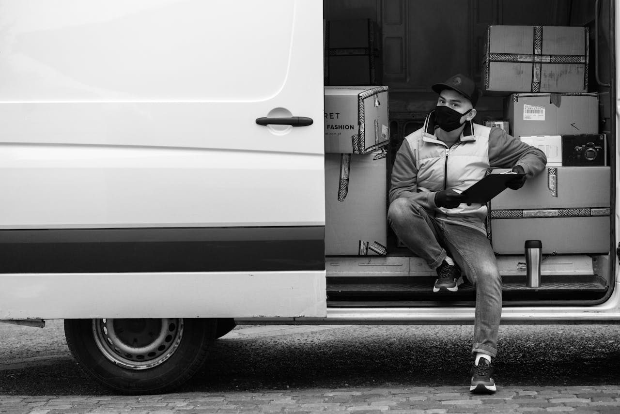 services-05 Masked courier sitting in delivery van holding a clipboard with packages, reflecting the new normal.